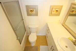 A small bathroom with a toilet, a sink, and a mirror. There are decorative frames on the wall above the toilet.
