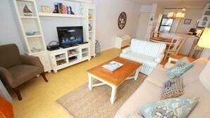 Una sala de estar con sofá, sillón, mesa de centro, televisor, estantería y un comedor con sillas y mesa.