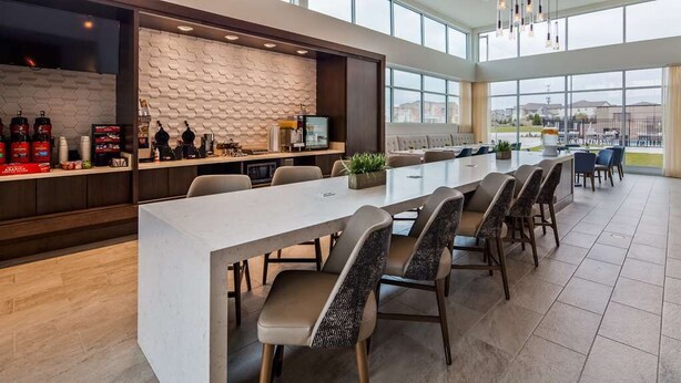 A modern kitchen area with a long counter, bar stools, and a seating area with a sofa and chairs. - Wingate by Wyndham Austin North (Austin)