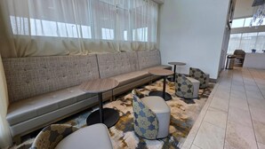 A seating area with a sofa and round tables, a patterned rug, and a view through sheer curtains. - Wingate by Wyndham Austin North (Austin)