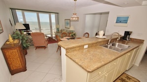 Un amplio salón con cocina, mesa de comedor y sillas. Una gran ventana ofrece vistas al océano.