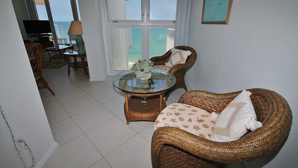 Una sala de estar con una mesa de vidrio, muebles de mimbre, vista al mar y un comedor con sillas y una mesa.