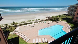 Ein Poolbereich mit Liegestühlen und Blick auf Strand und Meer.