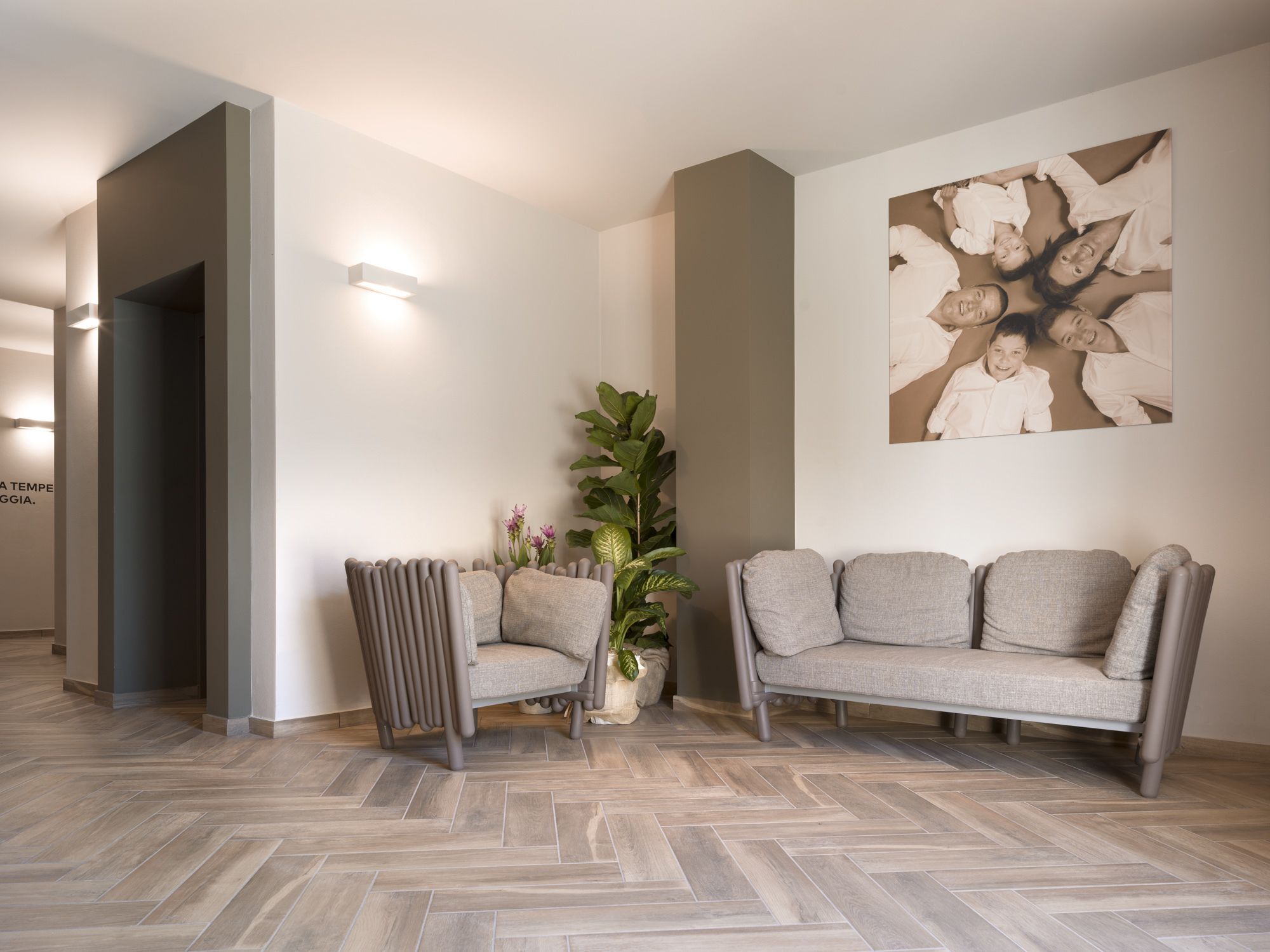 Ein modernes Wohnzimmer mit Fischgrätparkett, einem grauen Sofa, einem außergewöhnlichen Sessel, einem großen abstrakten Gemälde und einer Topfpflanze.