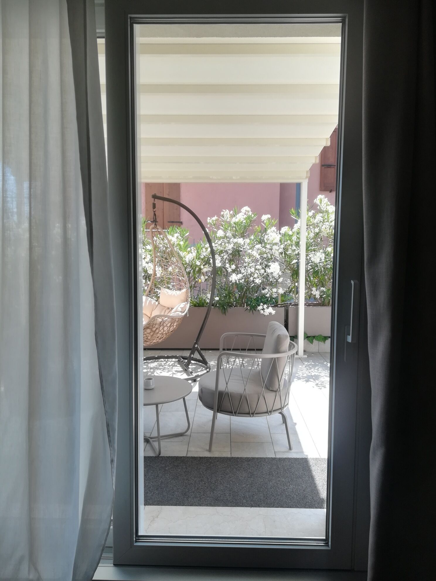 A sliding glass door leading to an outdoor patio with a cushioned chair, a small table, and a hanging chair.