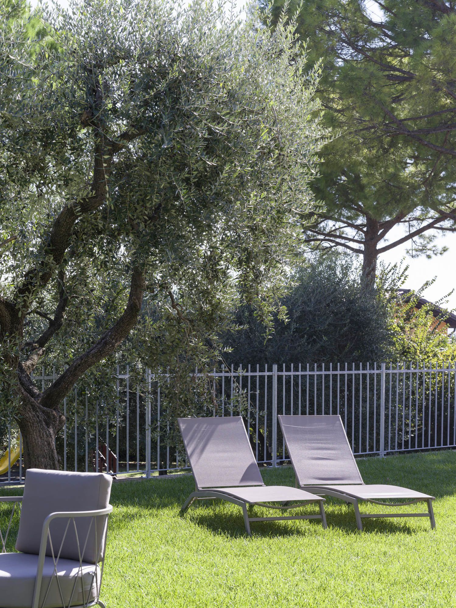 A grassy outdoor area with two lounge chairs and a metal fence.