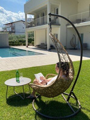 A person relaxing in a hanging chair by a pool, with a table and a bottle nearby. - L.A. Home (Moniga del Garda)