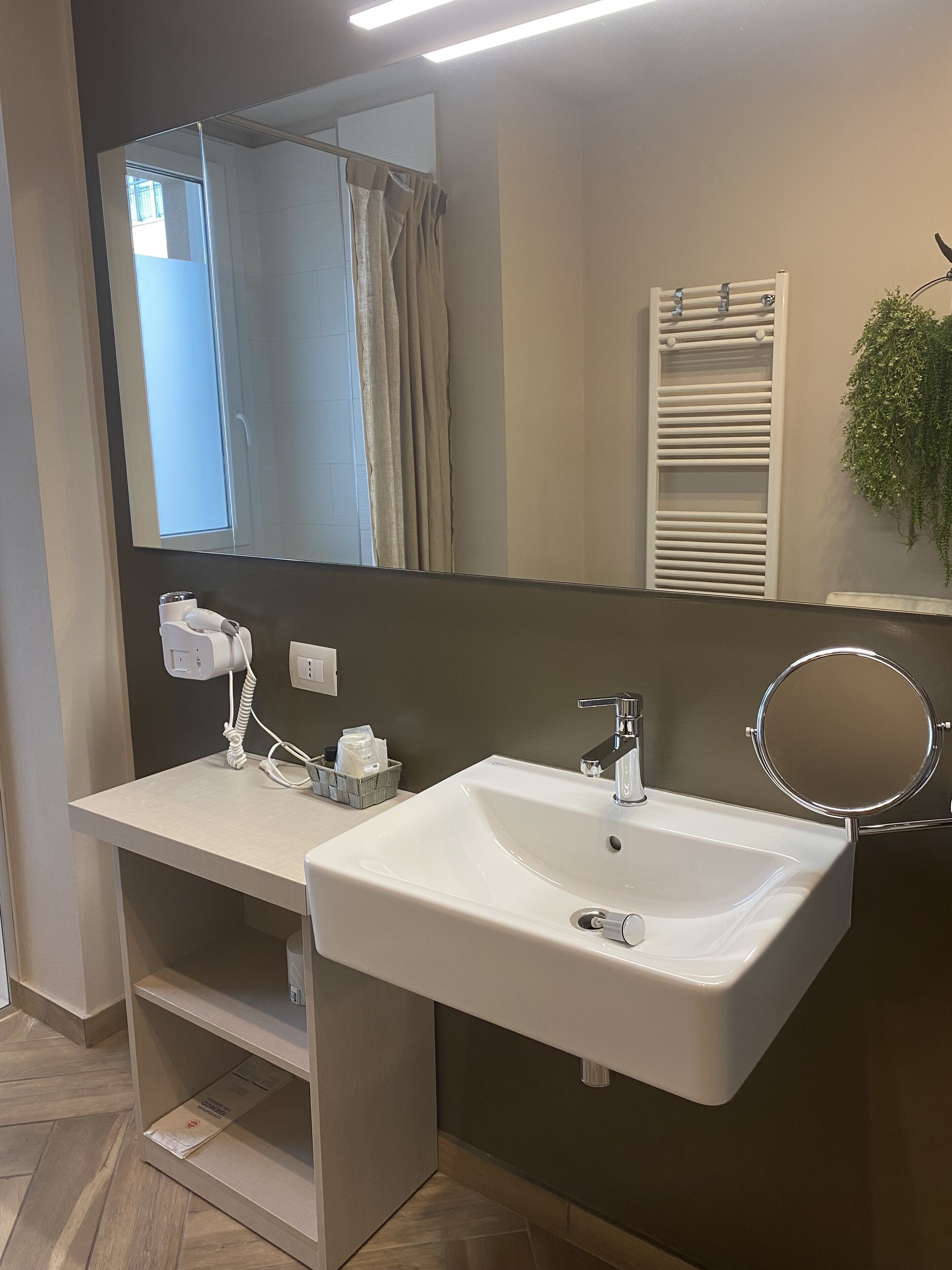 A modern bathroom with a white sink, a mirror, a towel rack, and a plant.