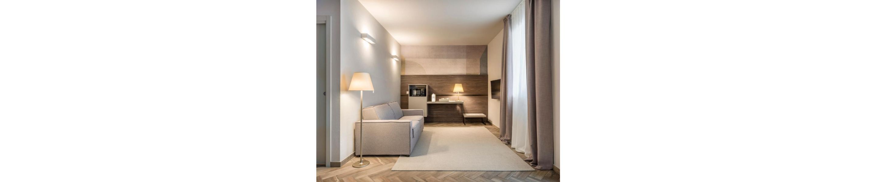 Un couloir d’hôtel moderne, avec un canapé, une lampe et une petite table.
