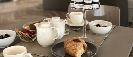 A breakfast setting with croissants, coffee cups, and jam jars on a table.