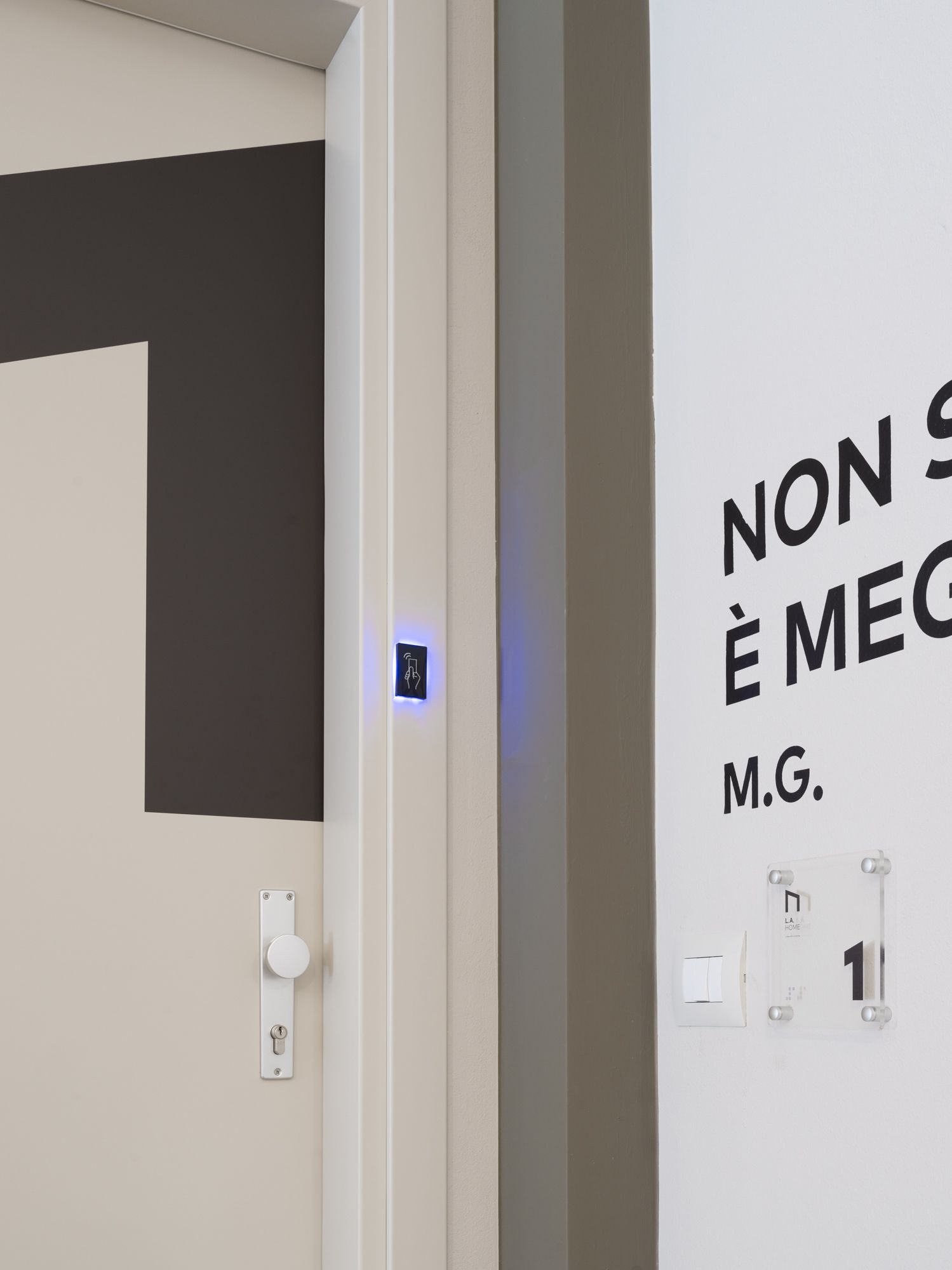 A modern bathroom with a minimalist design, featuring a toilet, a hand dryer, and a wall-mounted light switch.