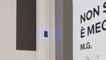 A modern bathroom with a minimalist design, featuring a toilet, a hand dryer, and a wall-mounted light switch.
