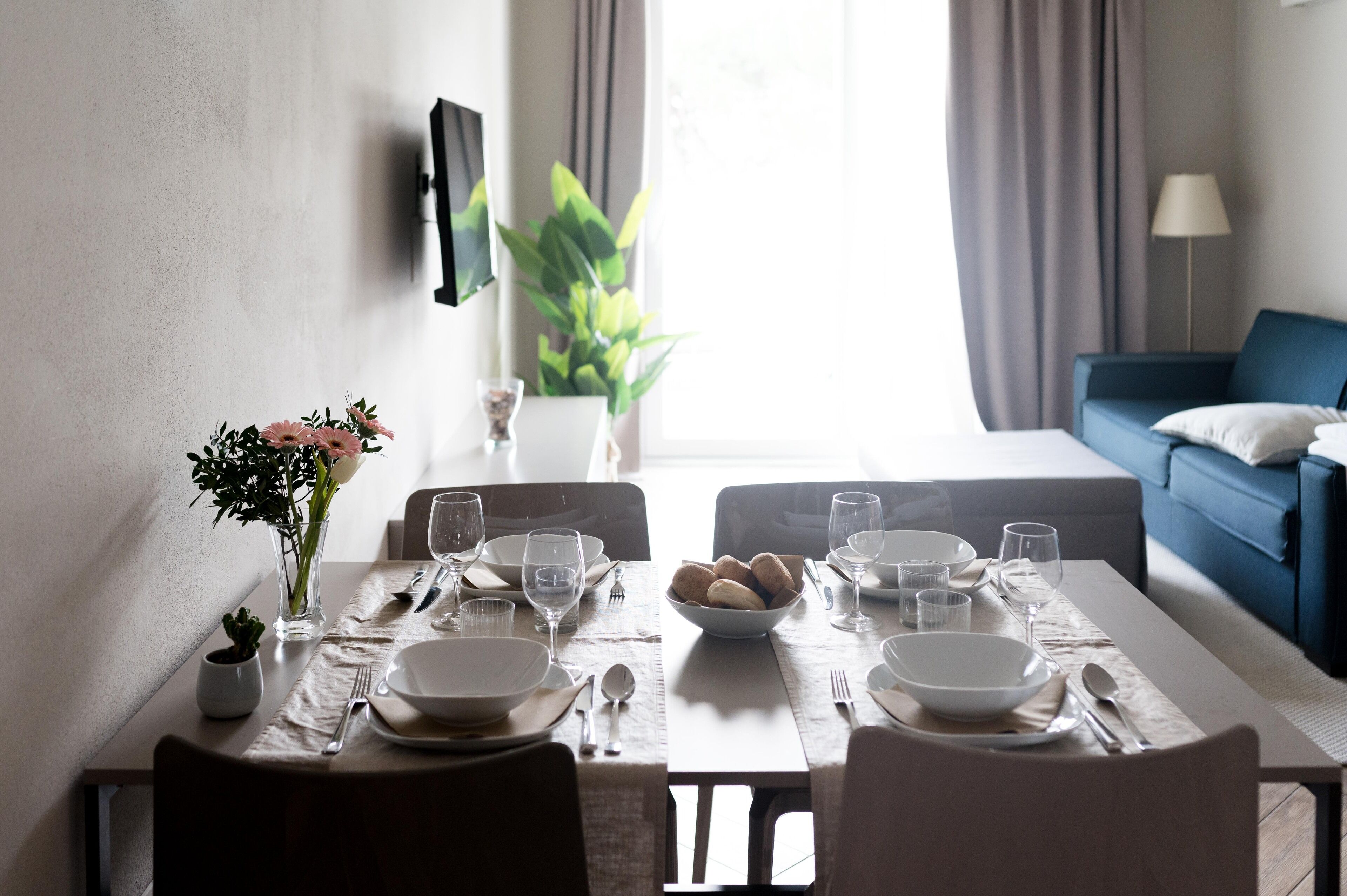 A dining table set with plates, bowls, and glasses, a vase with flowers, and a bowl of bread.