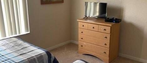 A bedroom with two beds, a wooden dresser, a painting on the wall, and a window with blinds.