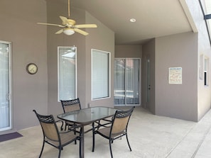 Eine überdachte Terrasse mit Tisch und Stühlen, einem Deckenventilator und einer Wanduhr.