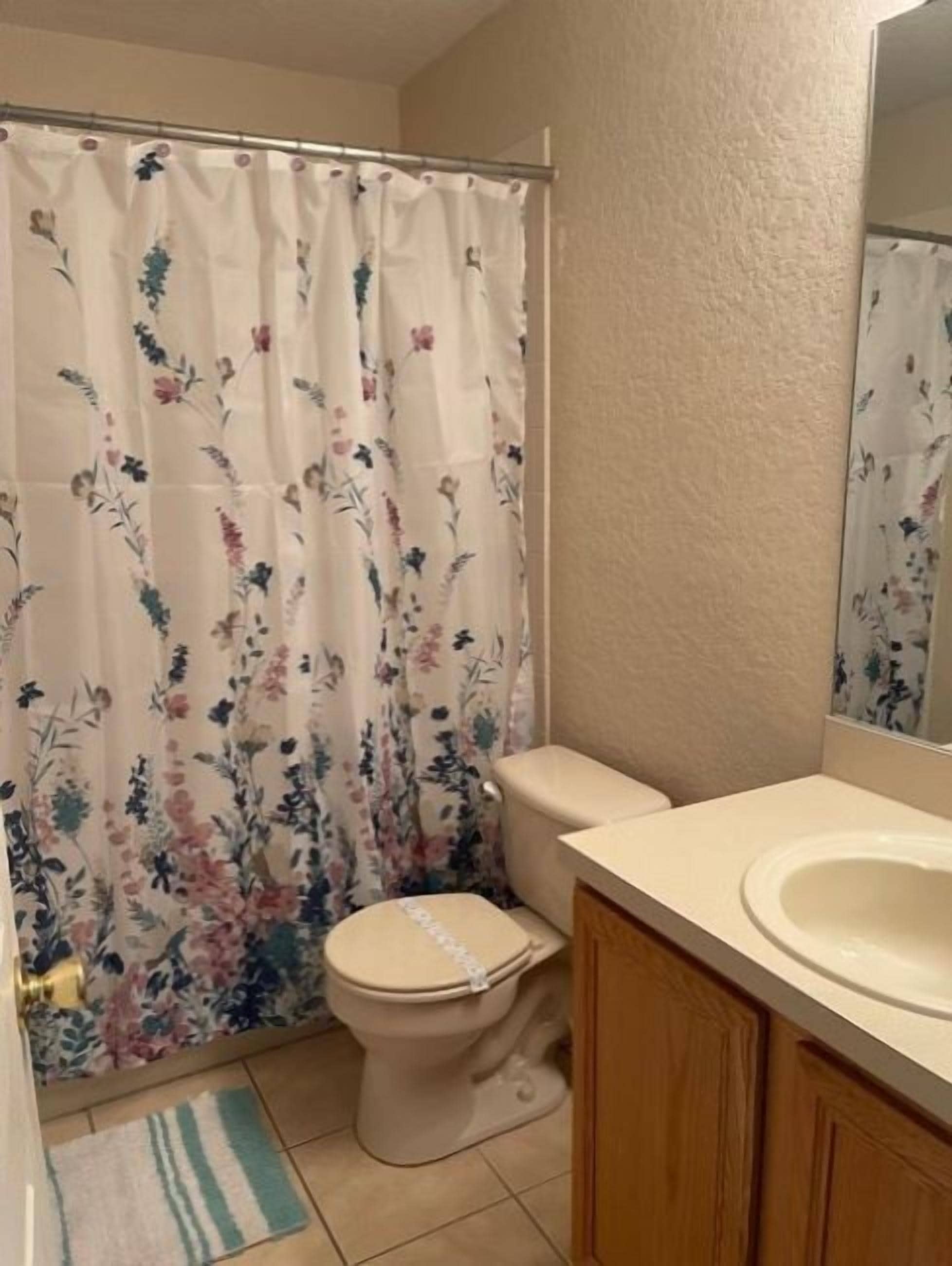 A bathroom with a toilet, a sink, a shower curtain with floral patterns, and a mirror above the sink.