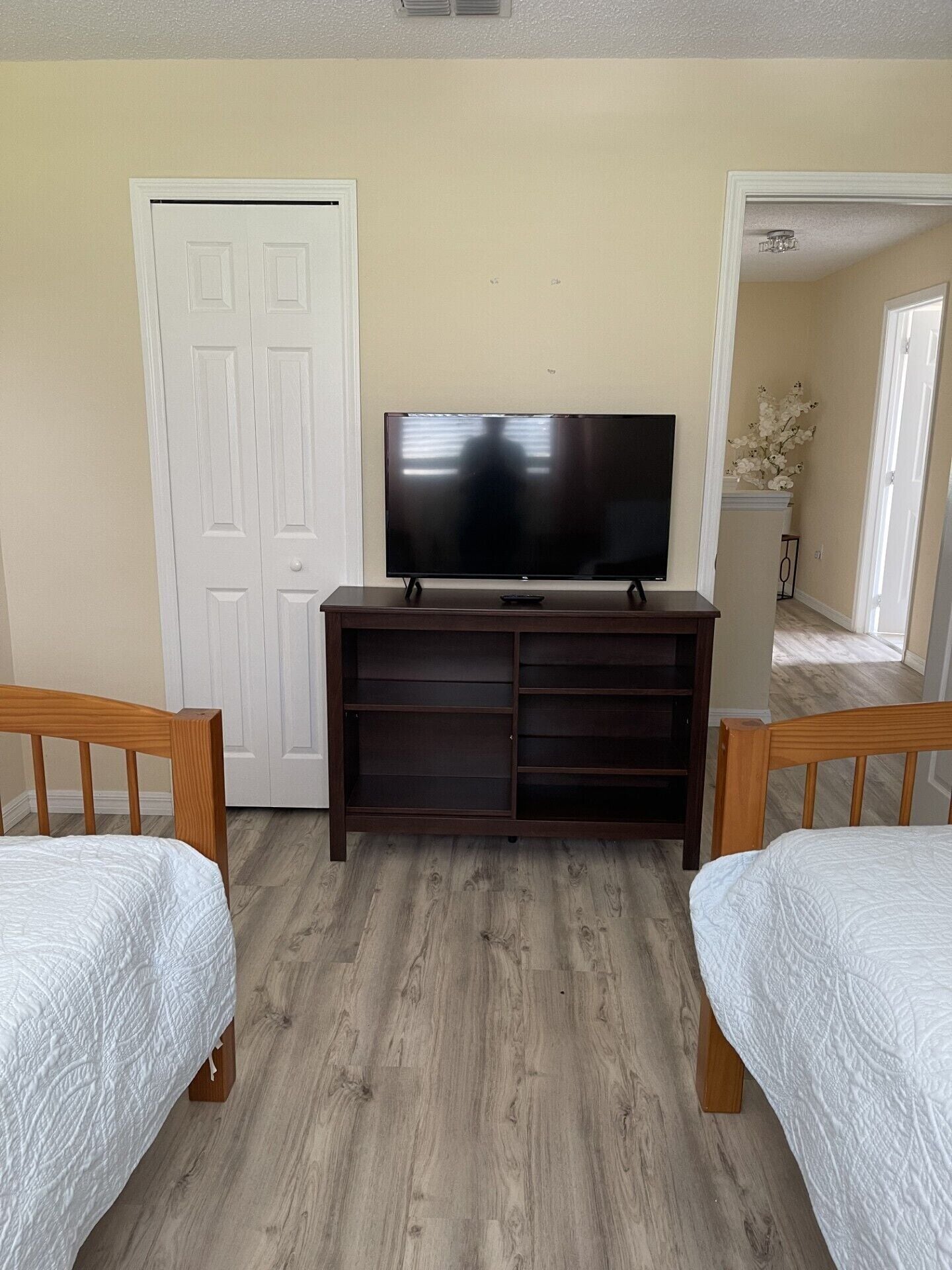 A bedroom with a TV on a stand, two beds, a wardrobe, and a door.