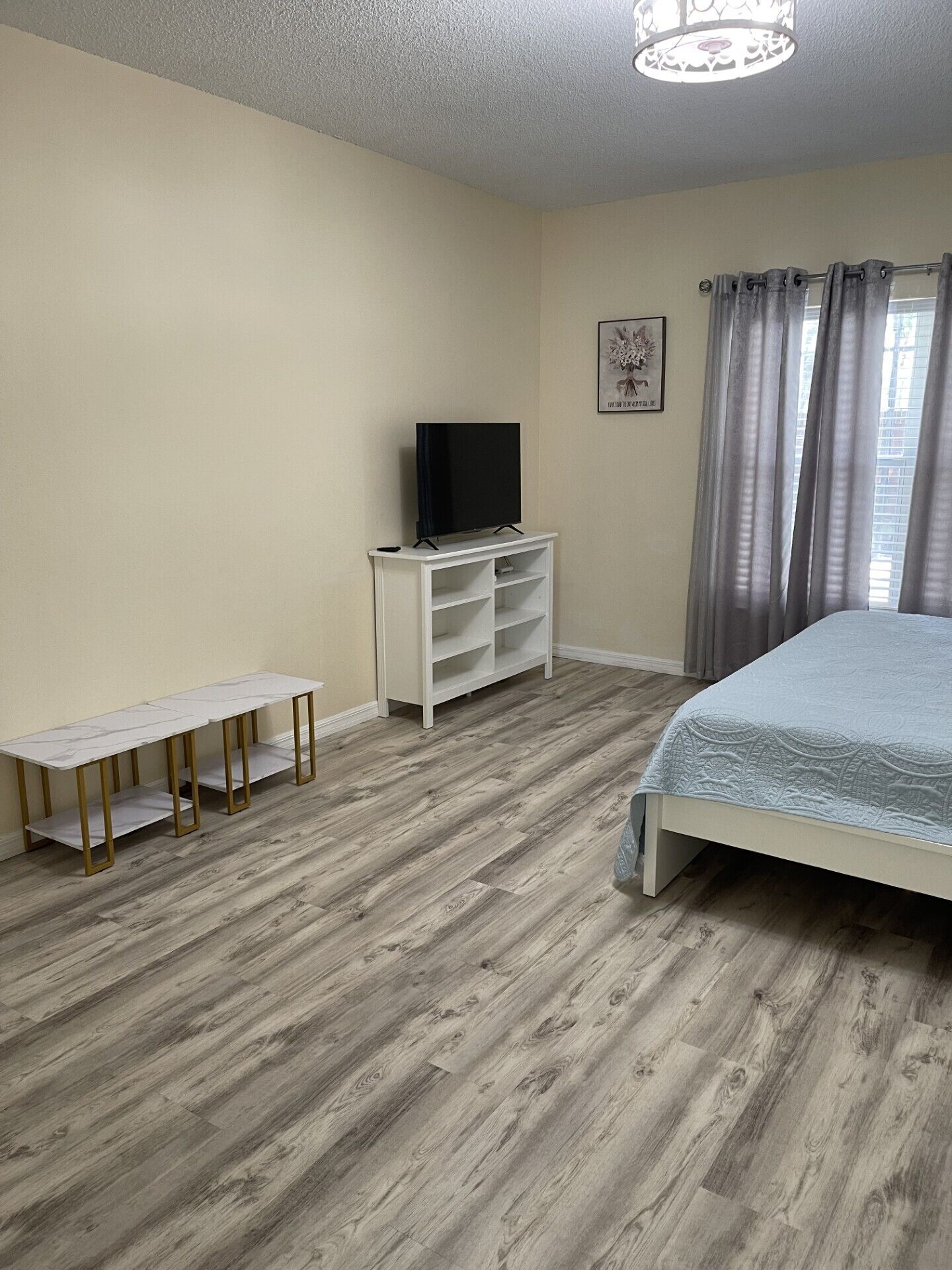 Een slaapkamer met een bed, een tv op een standaard, een bankje en een raam met gordijnen.