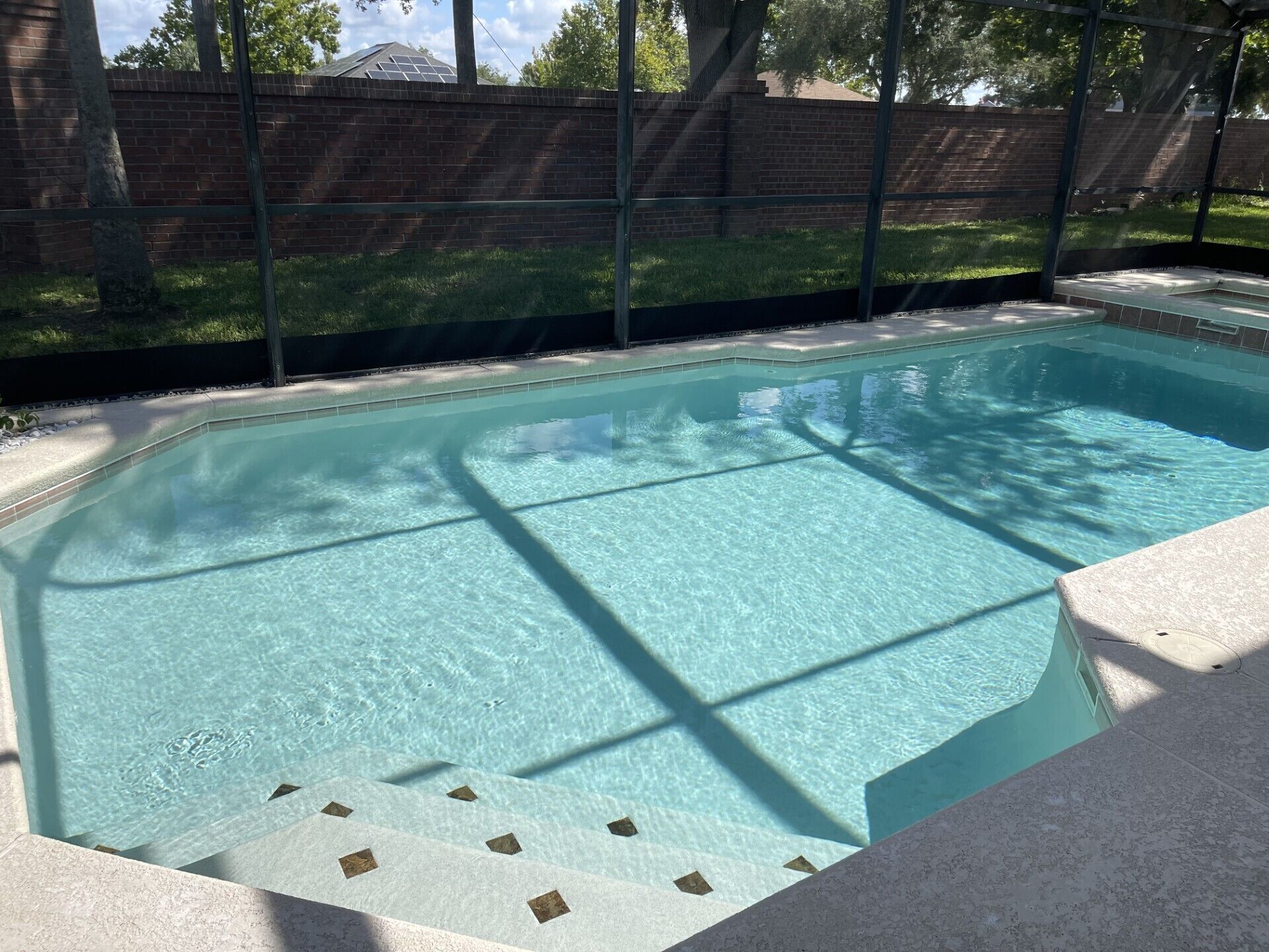 A rectangular swimming pool with clear water, surrounded by a brick wall and a metal fence.