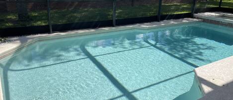 A rectangular swimming pool with clear water, surrounded by a brick wall and a metal fence.