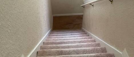 A carpeted staircase with a handrail, leading to a landing with a decorative wall piece.