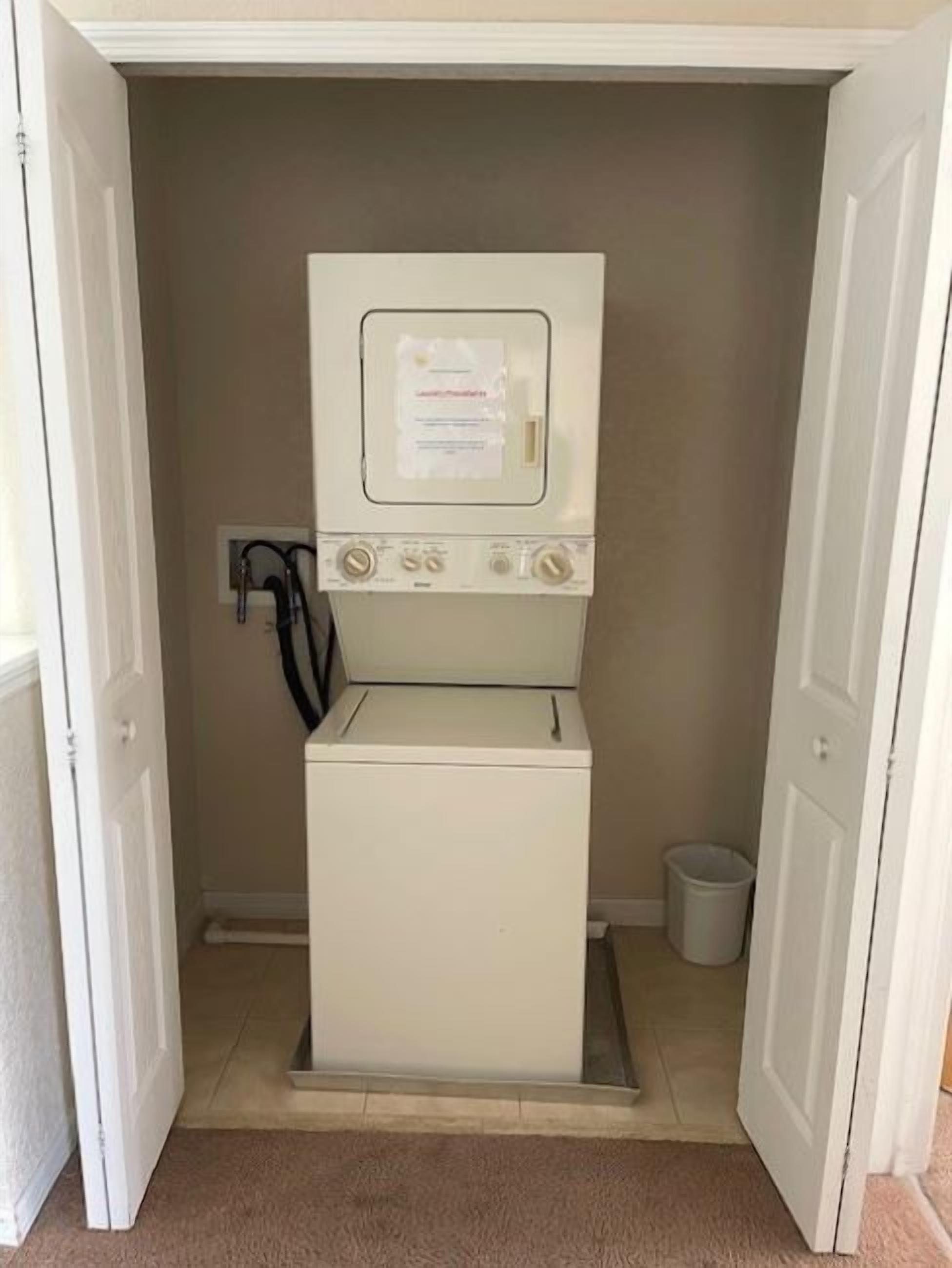 Une petite buanderie comprenant un lave-linge et un sèche-linge, une petite poubelle et une prise électrique au mur.