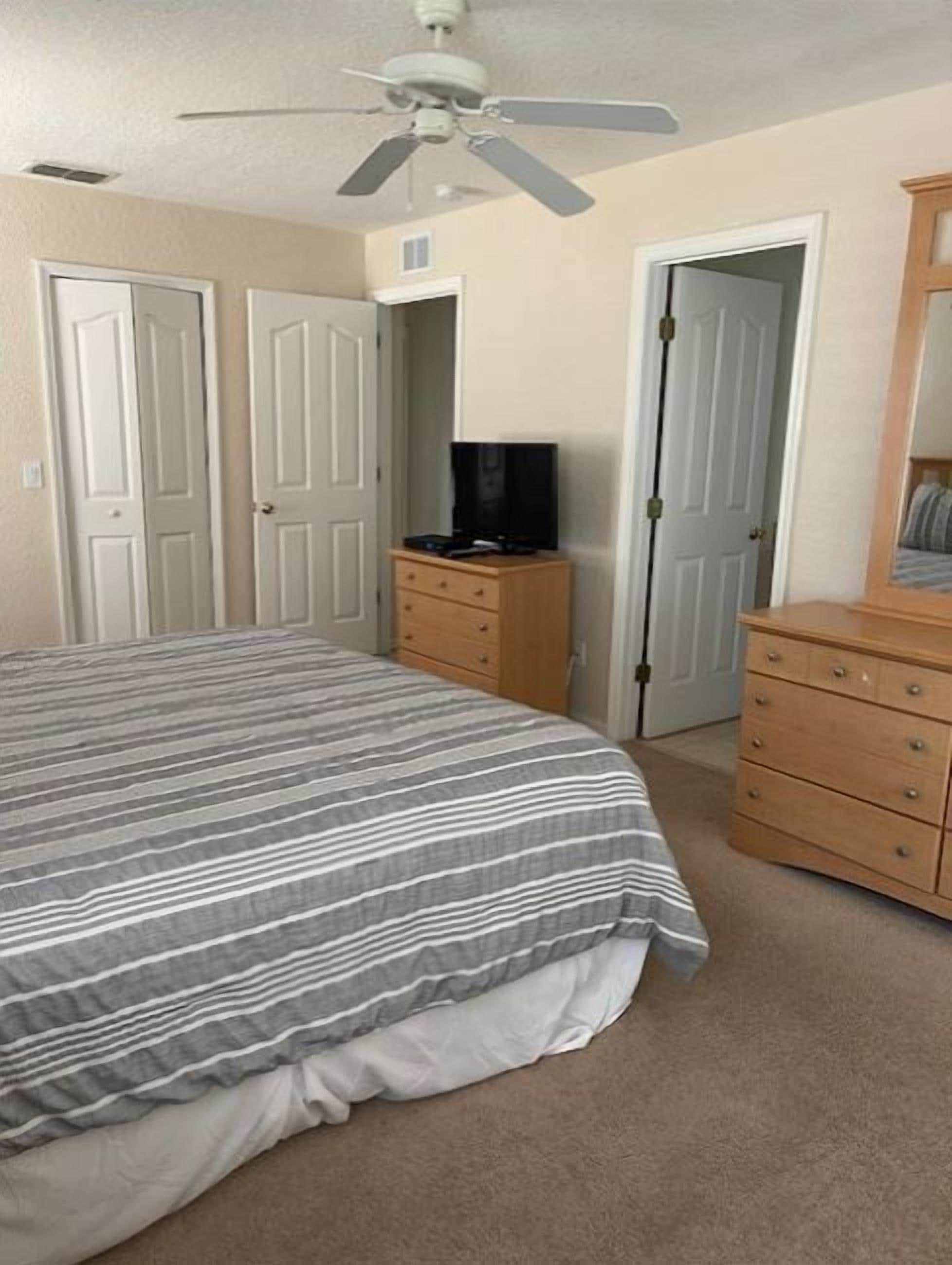 A bedroom with a bed, a dresser, a television on a stand, and a ceiling fan.