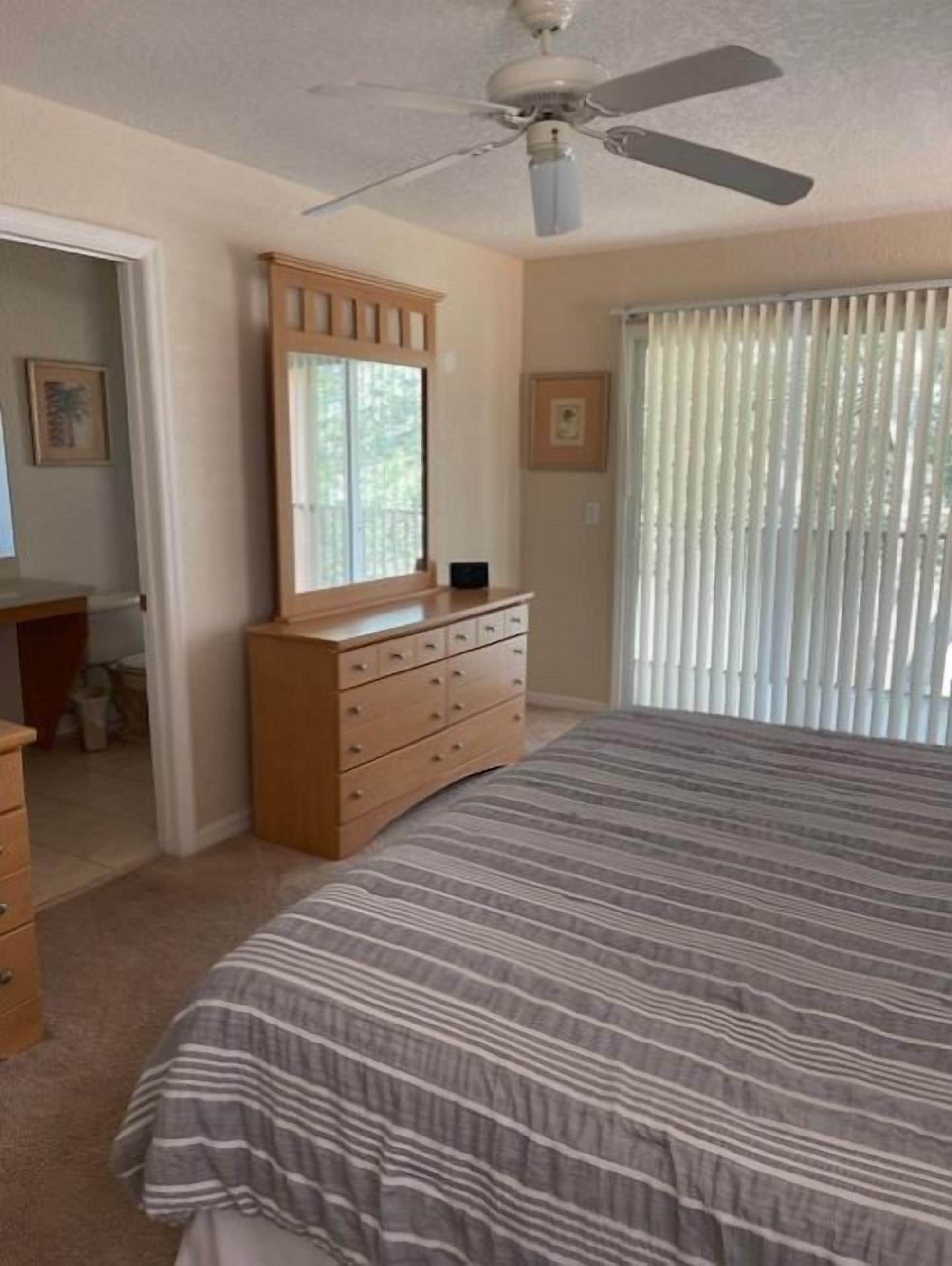 A bedroom with a bed, a dresser, a ceiling fan, and a window with blinds.