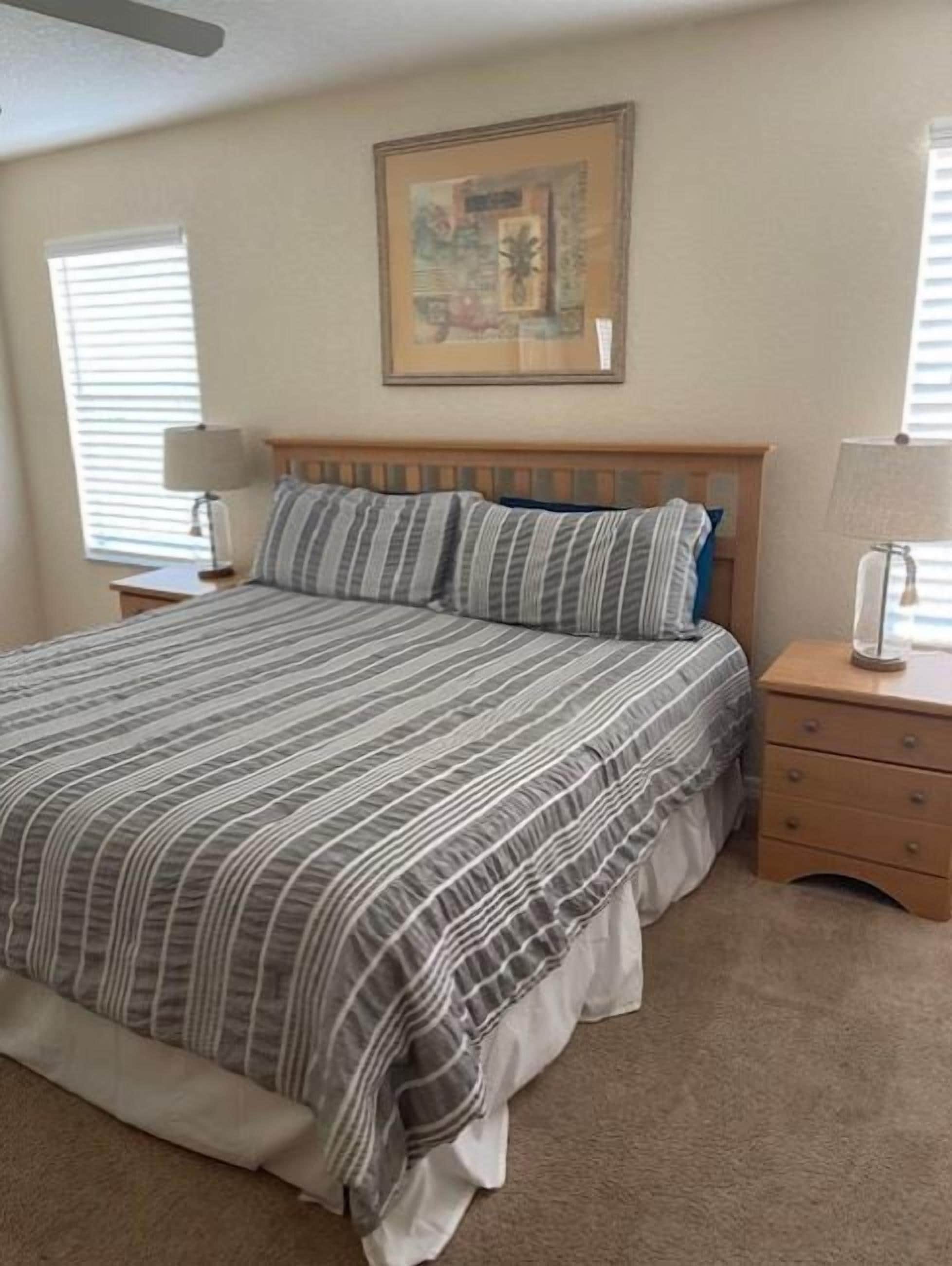 A bedroom with a bed, a nightstand, a dresser, and a wall-mounted picture.