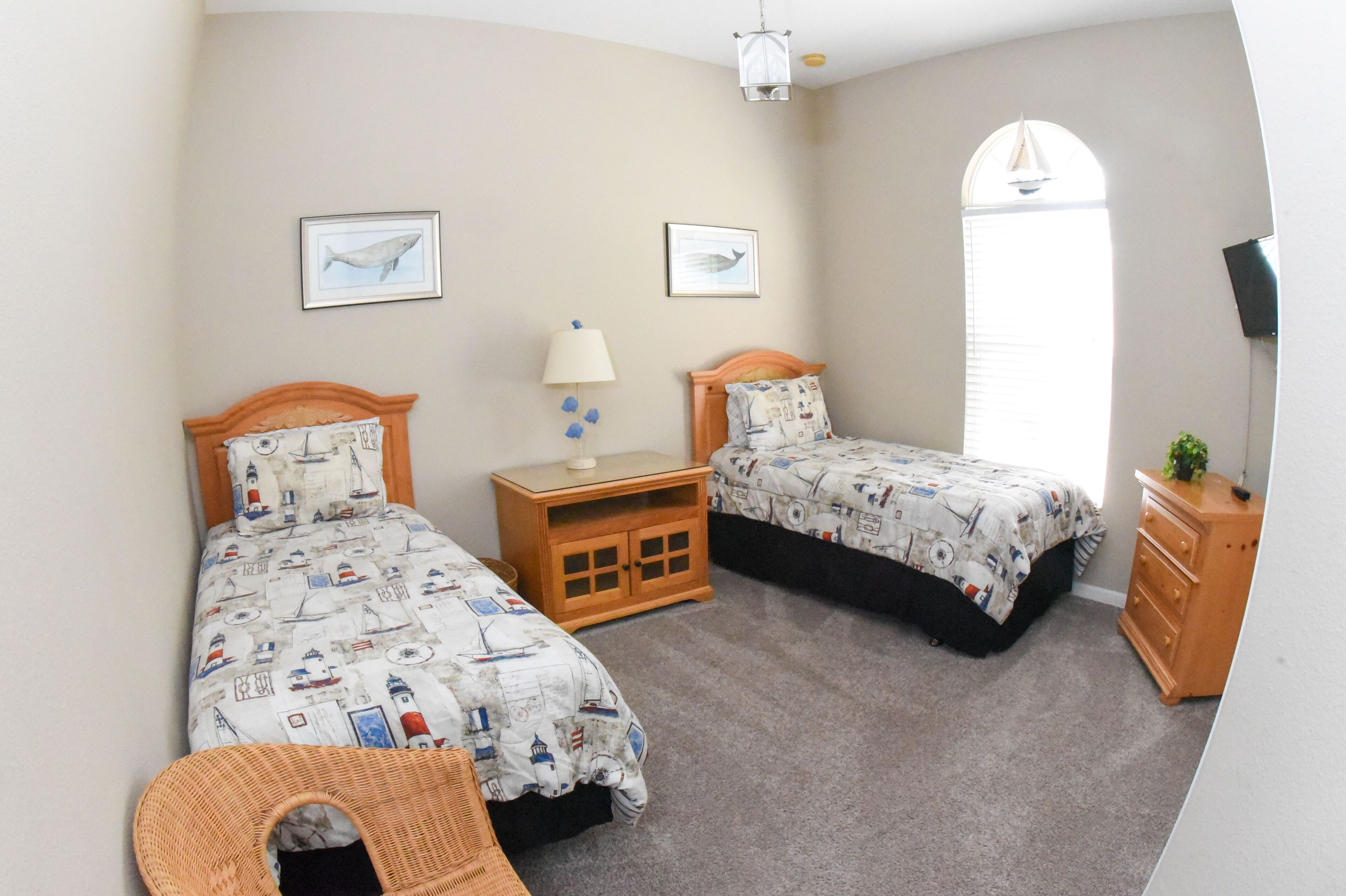 A bedroom with two single beds, a nightstand, a dresser, a lamp, and two framed pictures on the wall.