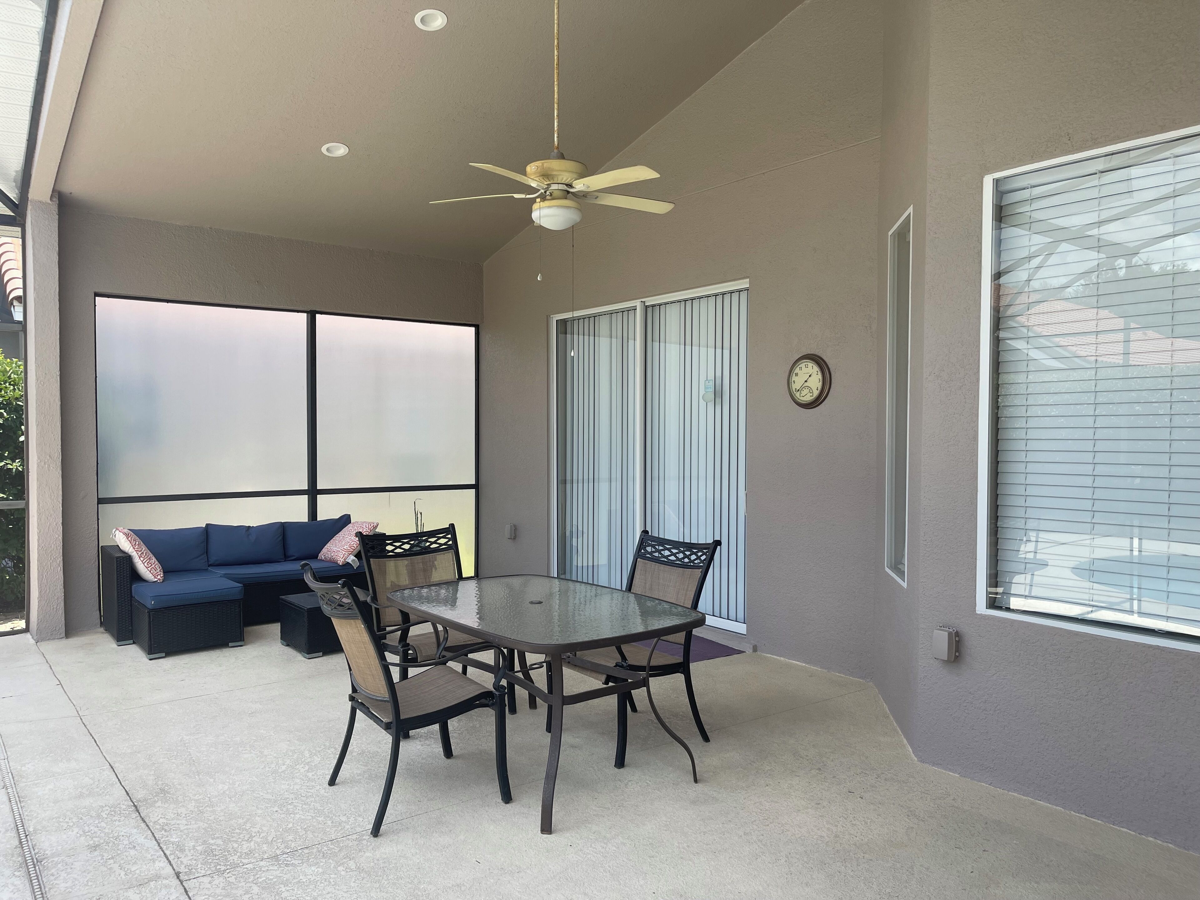 A covered patio area with a glass table and chairs, a blue sofa, and a ceiling fan.