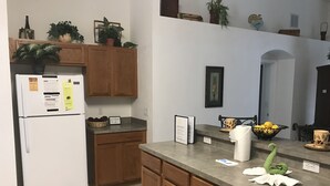 A kitchen with wooden cabinets, a refrigerator, and a countertop with a basket of lemons and a bowl of fruit.