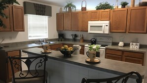 A kitchen with wooden cabinets, a microwave, a stove, and a sink. There are chairs and a table with a bowl of fruit.