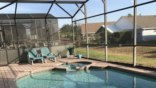 A swimming pool with a brick deck, lounge chairs, and a covered seating area.