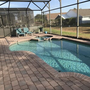 Une piscine entourée d’une terrasse en briques, avec des chaises longues et un espace salon abrité.