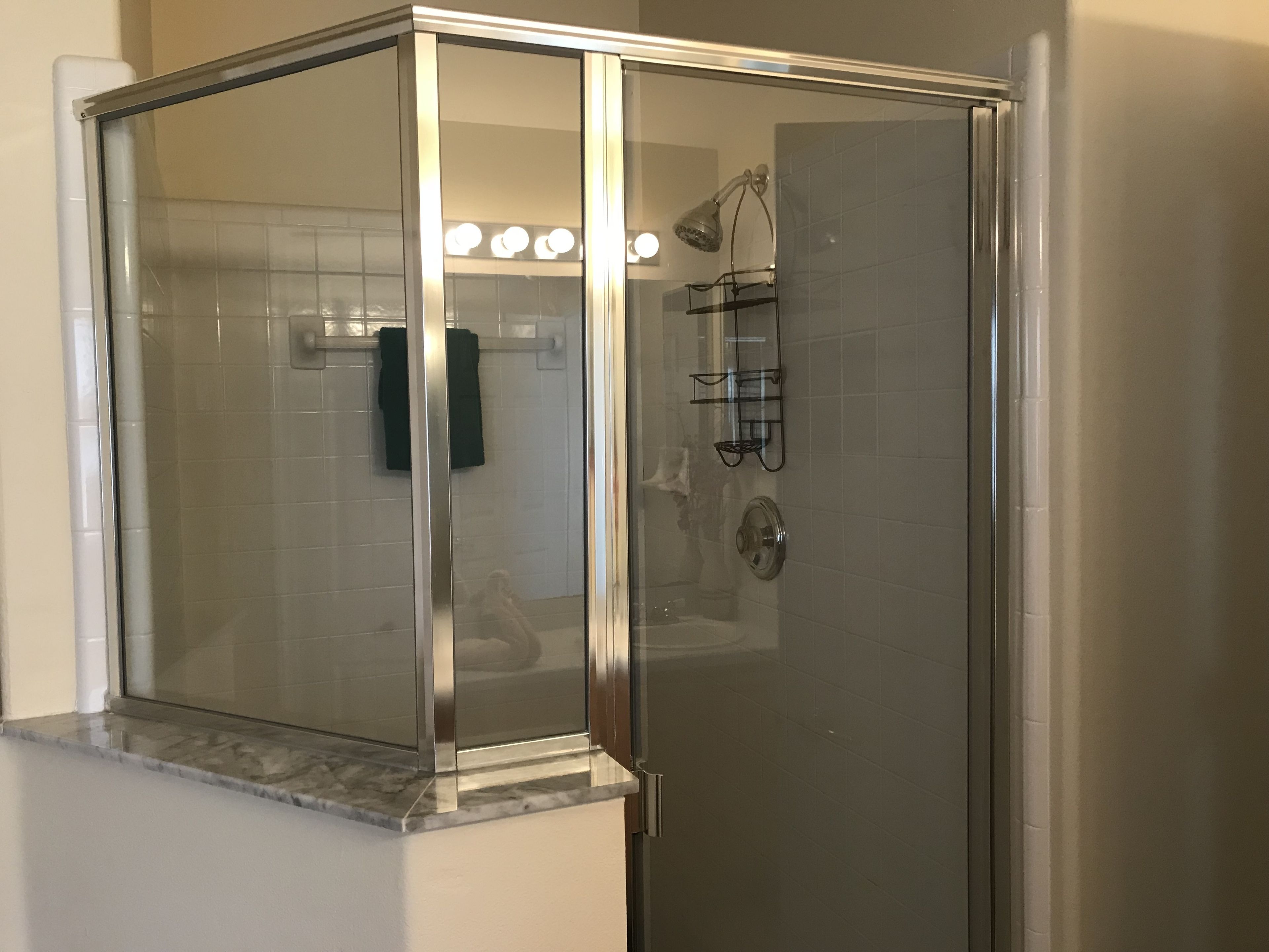 A glass-enclosed shower with a marble ledge, a towel rack, and a glass door.