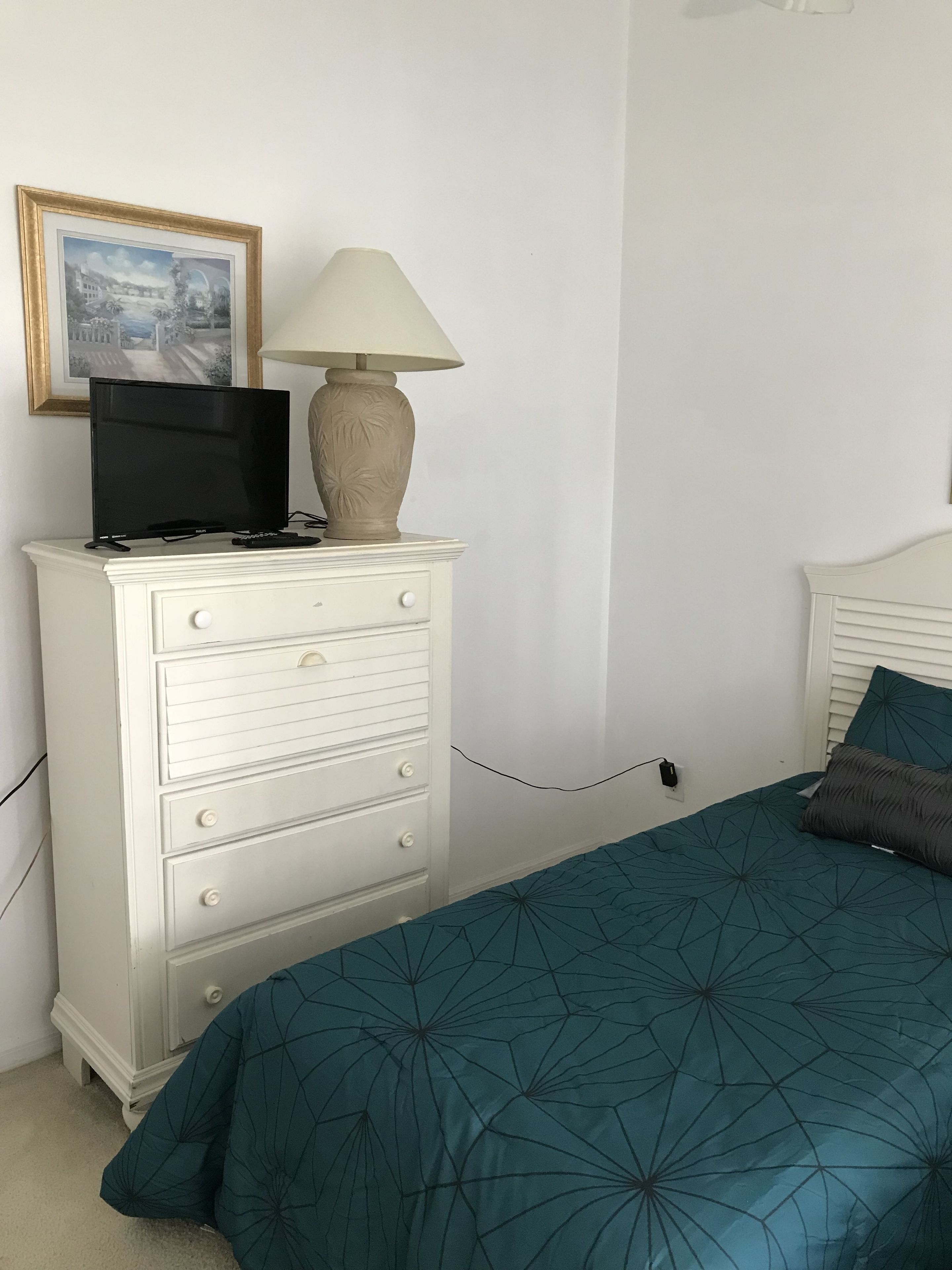 A bedroom with a bed, a dresser with a television and lamp, and a framed picture on the wall.