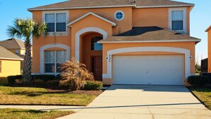 A two-story house with a garage, a small front yard with a palm tree, and a clear blue sky.