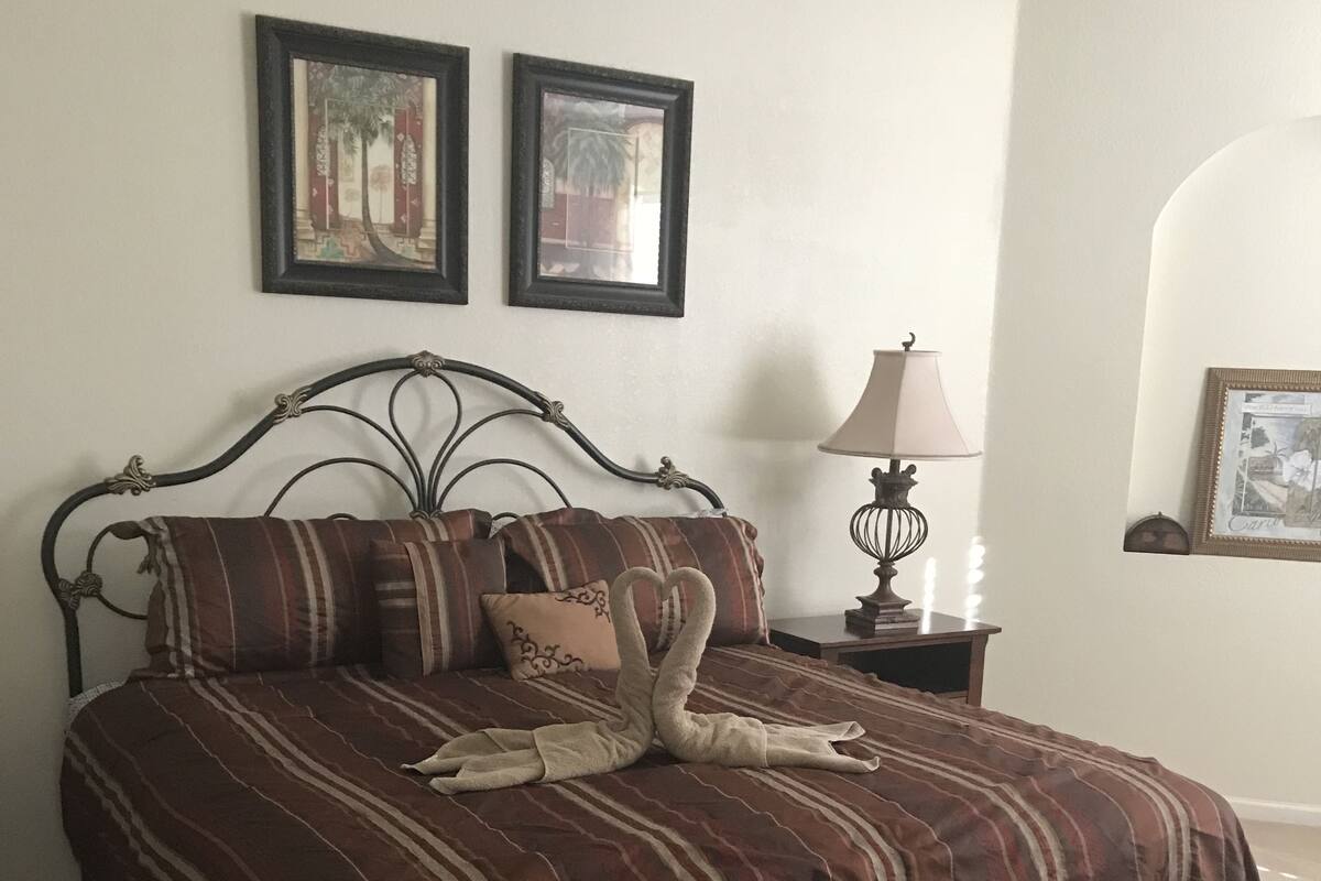 Una cama con una colcha a rayas y dos almohadas, una mesita de noche con una lámpara, y dos cuadros enmarcados en la pared.
