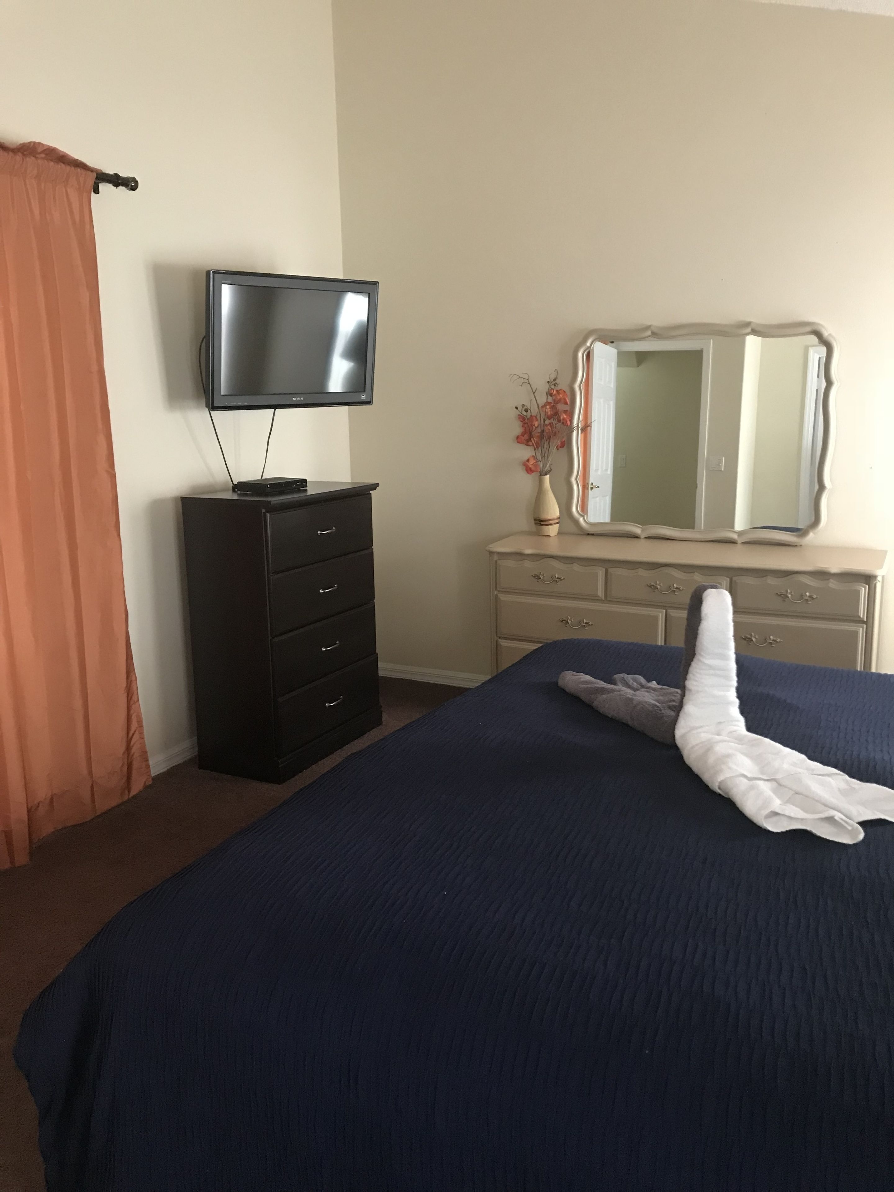 A hotel room with a bed, a TV, a dresser, and a mirror.