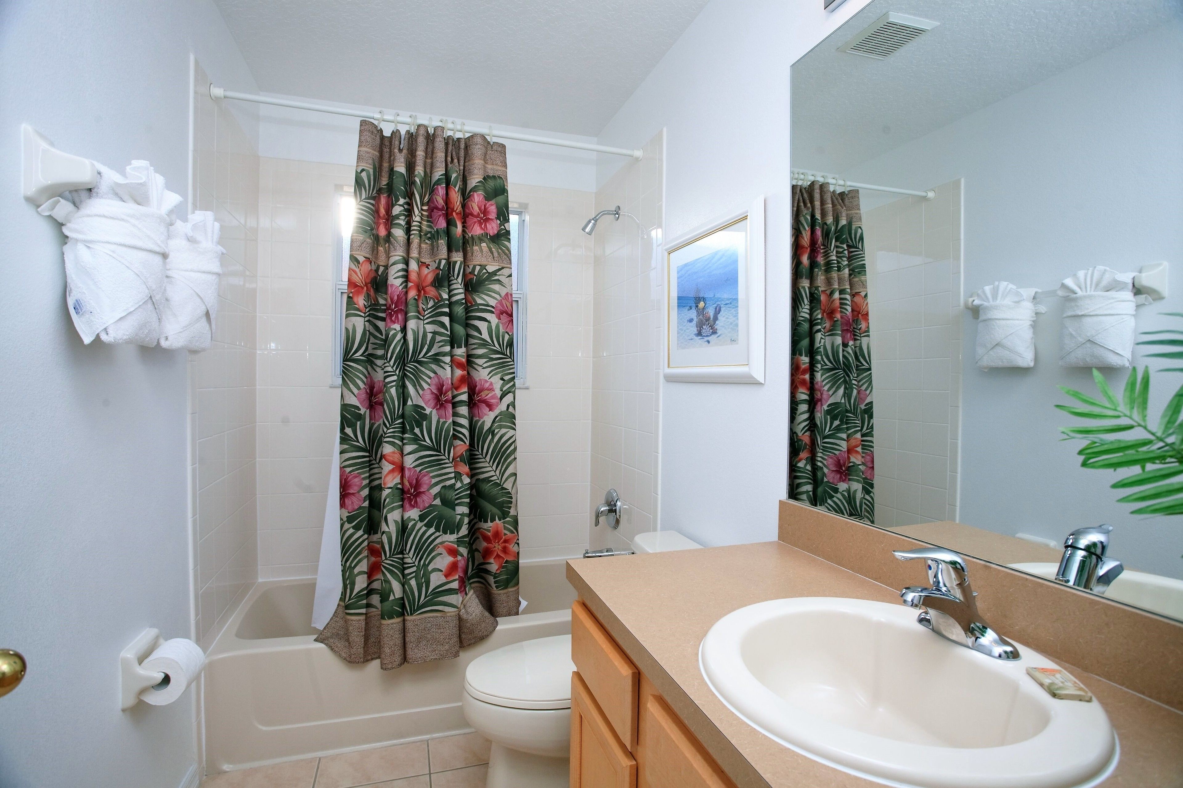 Een badkamer met een bad, toilet, wastafel en douchegordijn met een bloemenprint.