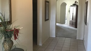 A hallway with tiled flooring, a glass table with a plant, a mirror, and a door leading to another room.