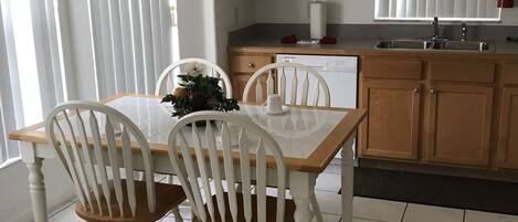 A kitchen with a dining table, chairs, cabinets, a dishwasher, and a window with blinds.