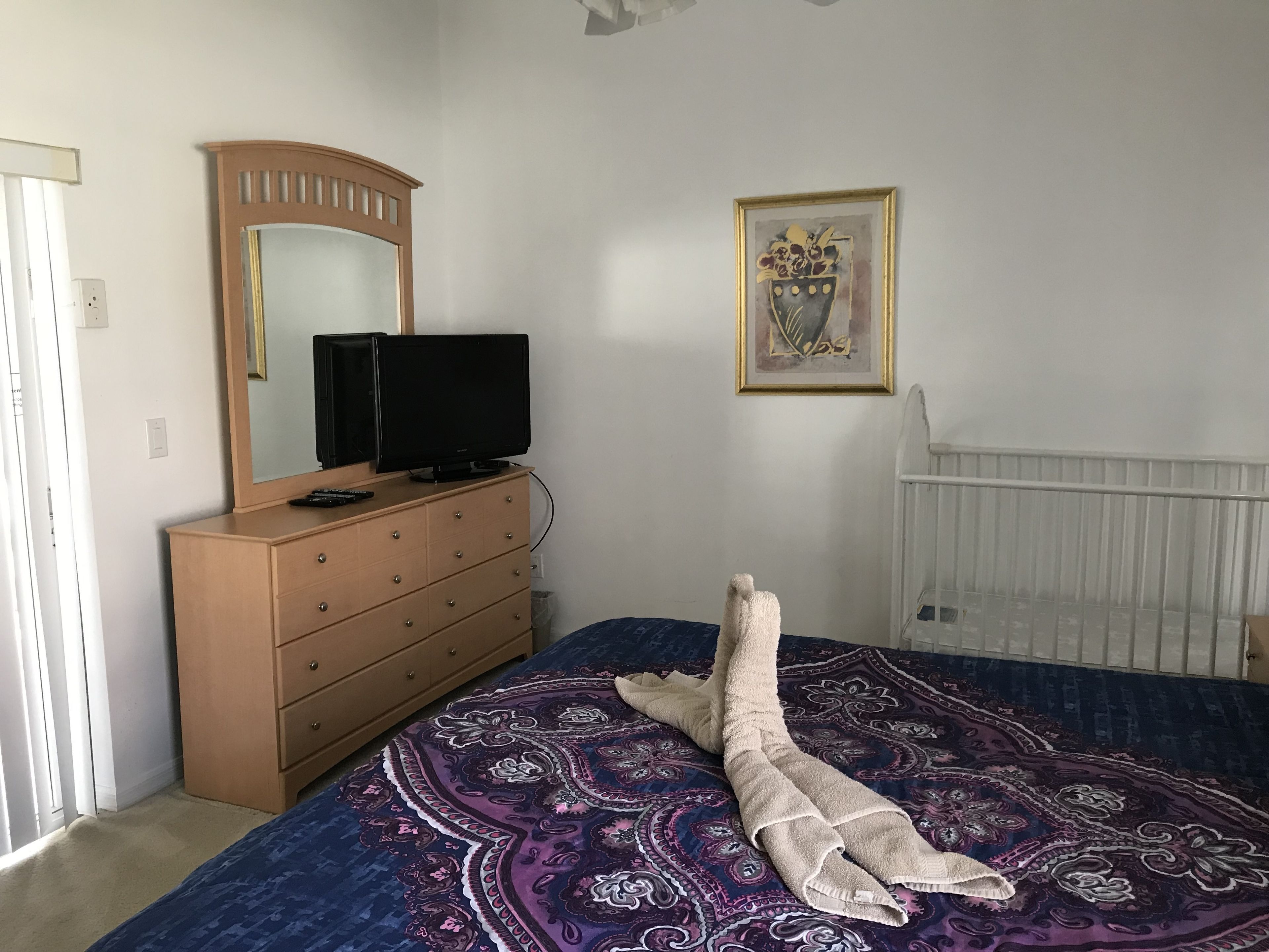 A bedroom with a bed, a dresser, a television, a framed artwork, and a radiator.
