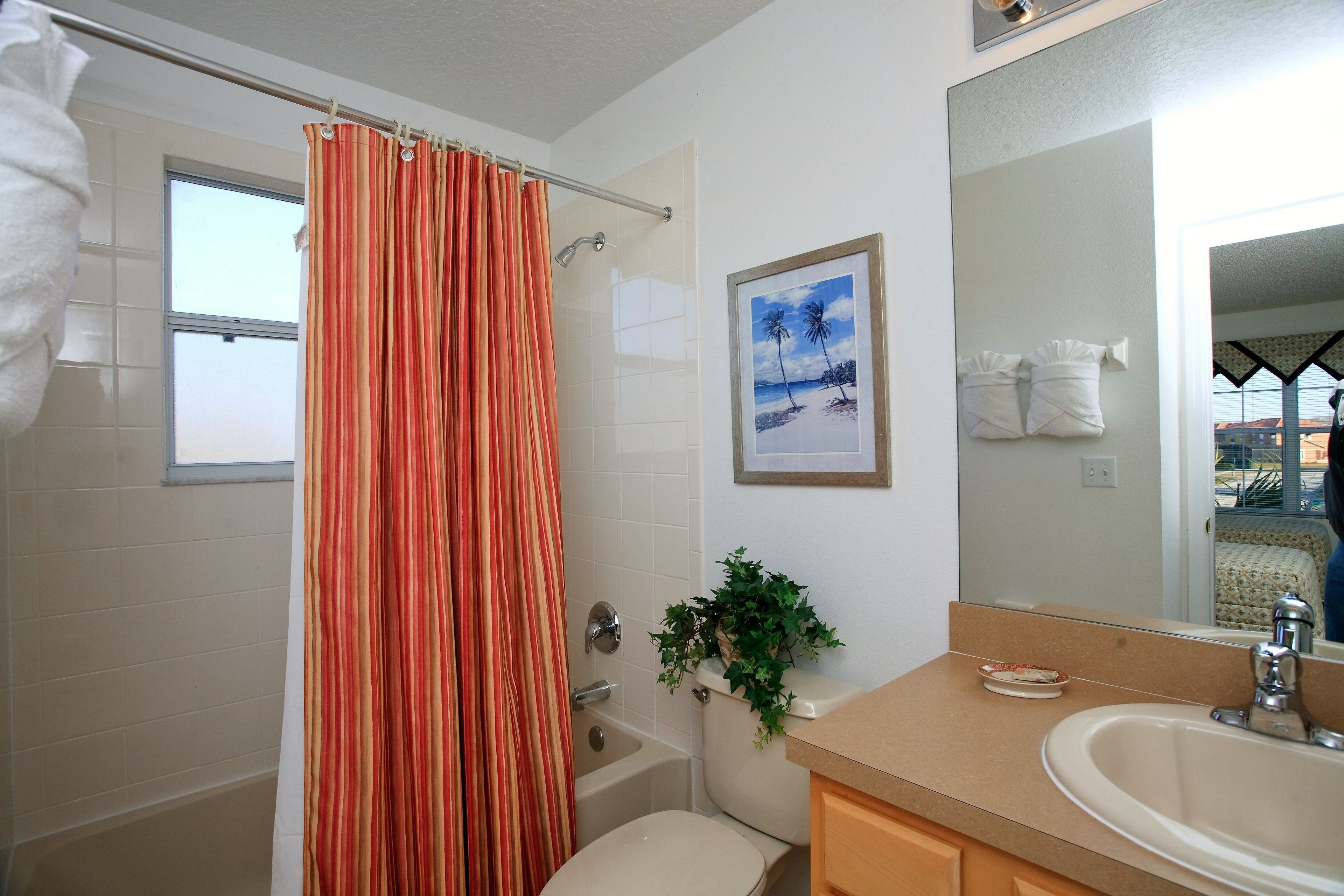 Une salle de bain avec un rideau de douche, des toilettes, un lavabo, un miroir et un tableau encadré au mur.