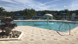 A swimming pool with blue chairs and umbrellas, surrounded by a tiled deck and palm trees.