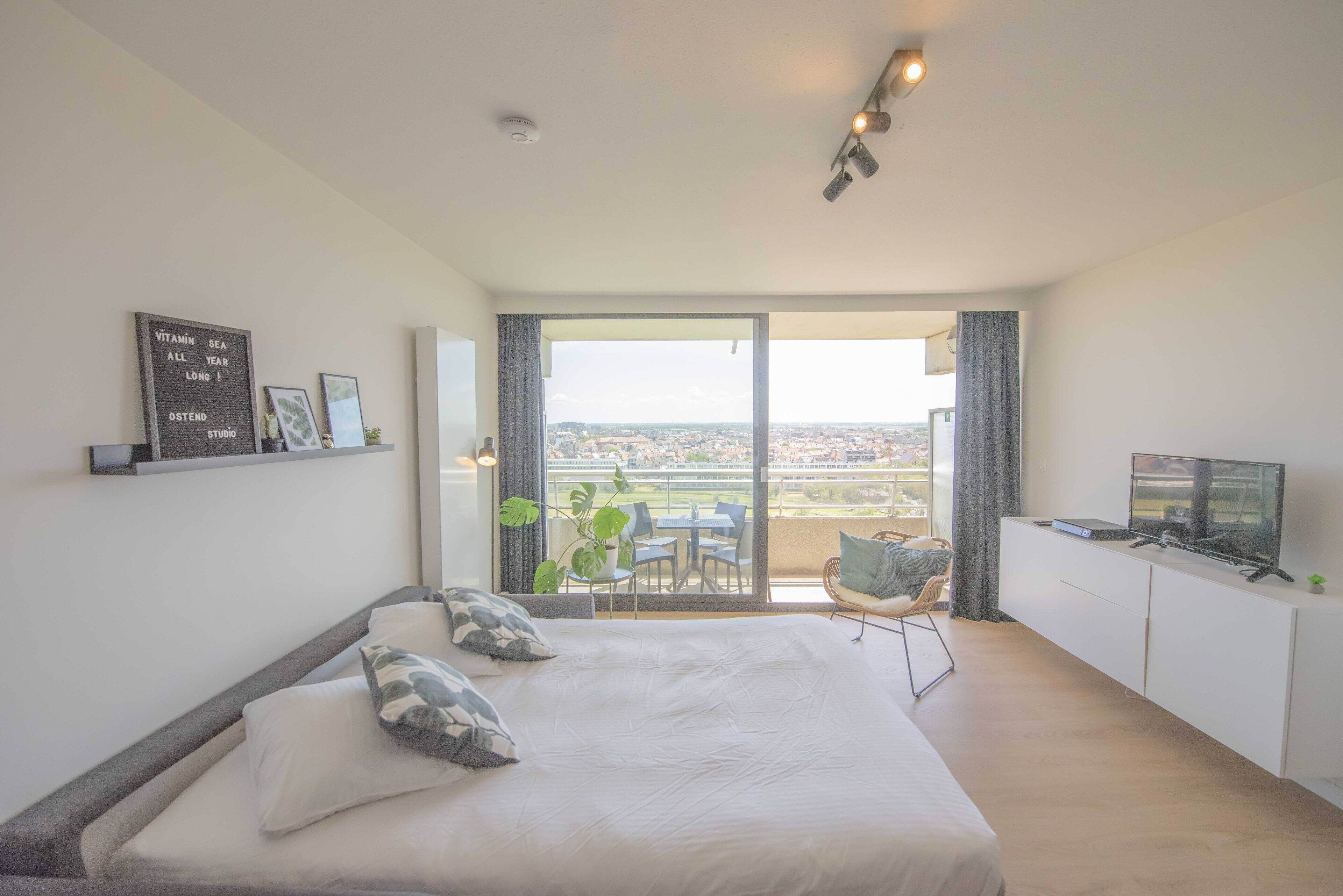 Une chambre d’hôtel moderne dotée d’un grand lit, d’une télévision et d’un balcon offrant une vue sur la ville.