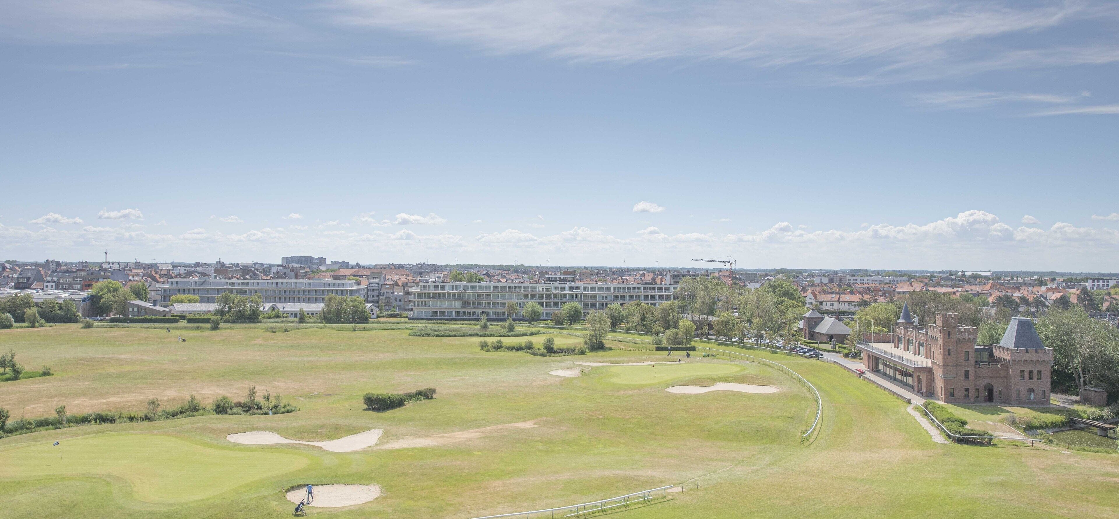 Un parcours de golf avec des bunkers et, au fond, un grand bâtiment à l’architecture rappelant celle d’un château.