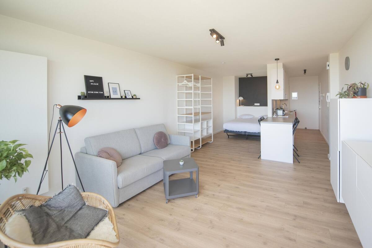 Un salon moderne avec un canapé, une petite table, une lampe sur pied et un téléviseur posé sur un meuble.