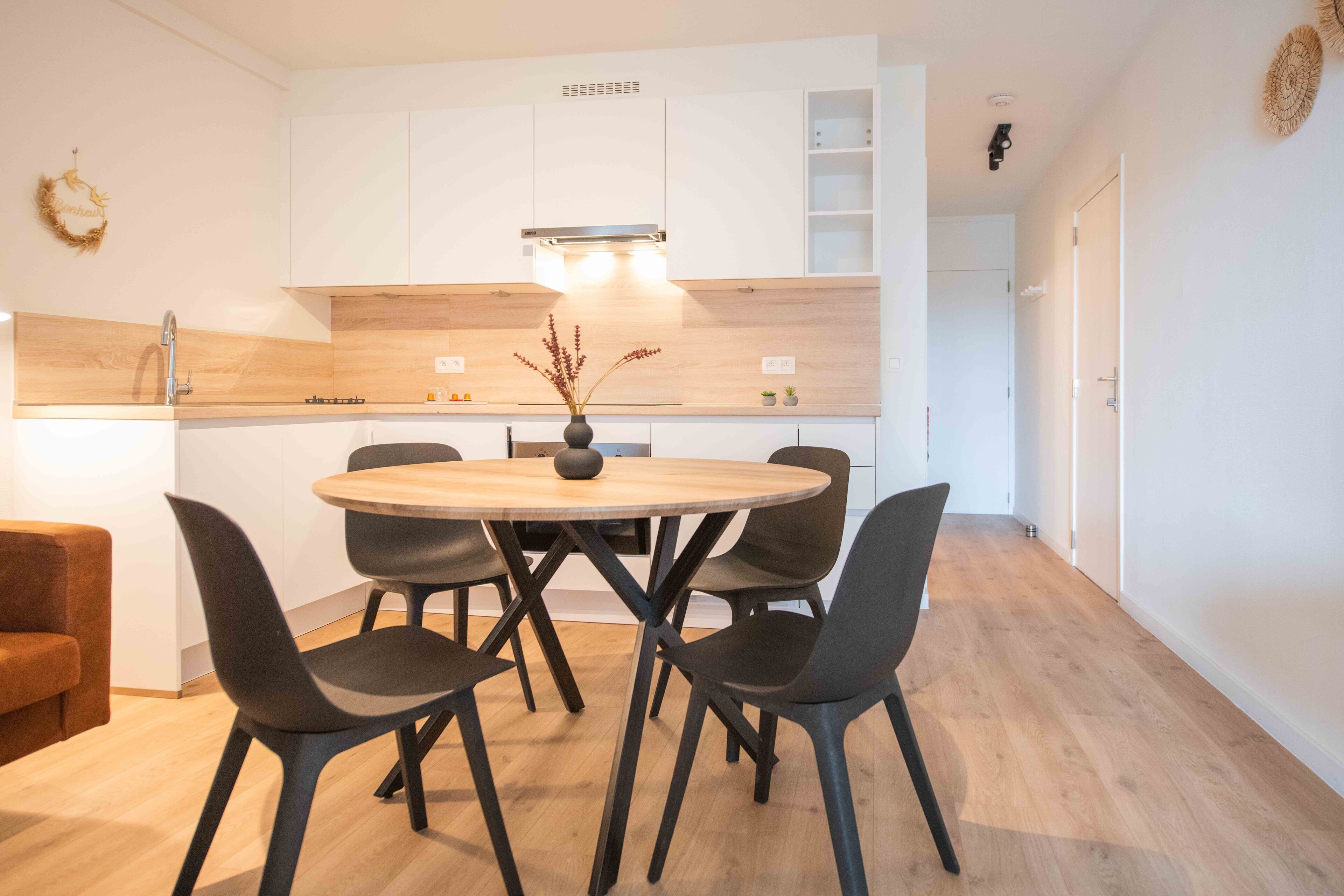 A modern kitchen with white cabinets, a wooden countertop, and a round dining table with black chairs.